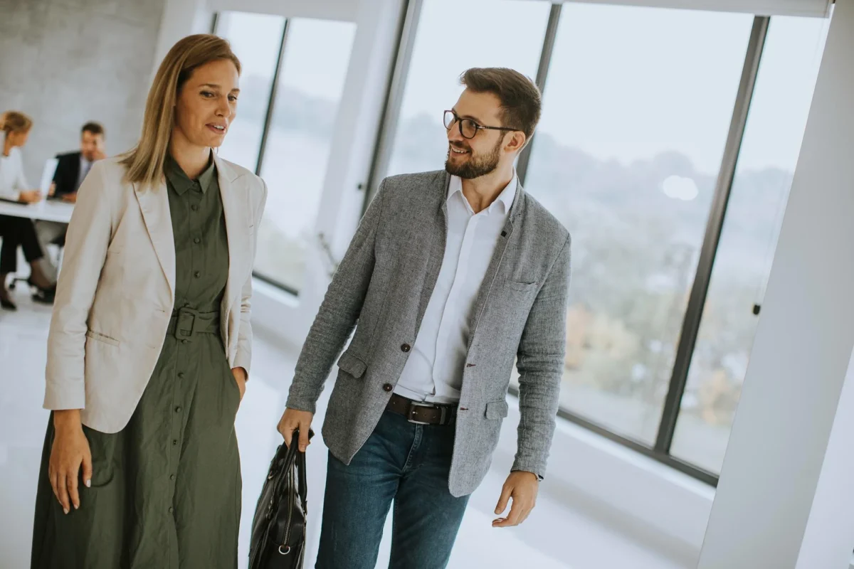 Two colleagues talking while walking through a bright office with large windows
