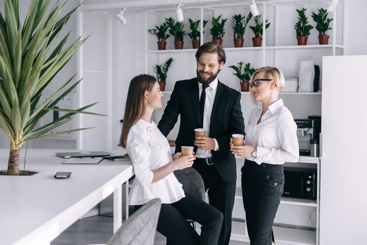 Three colleagues with coffee talking in a bright office kitchen